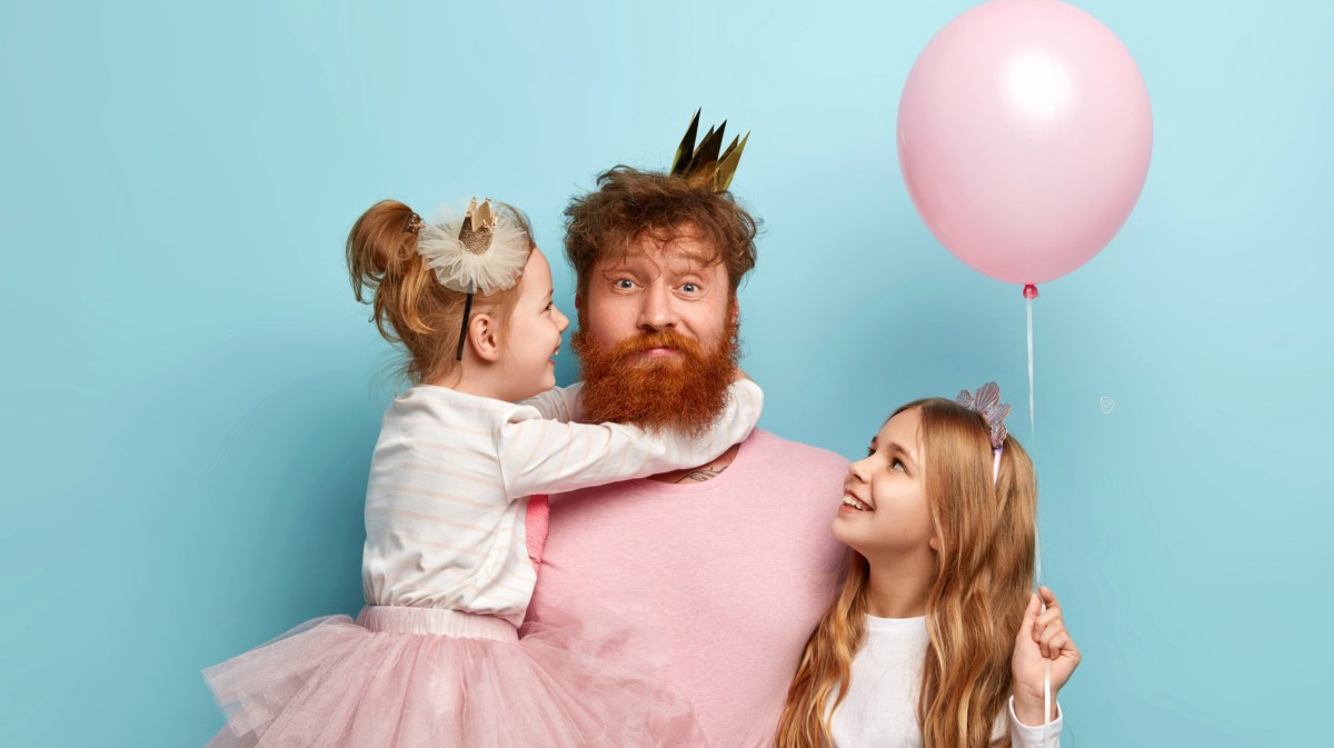 Vater mit zwei Kindern vor einer blauen Wand, der eine Krone aufhat und einen Ballon in der Hand hält.