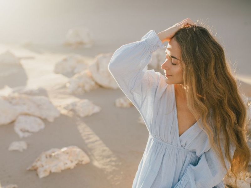 Frau bei Sonnenschein am Strand, die sich lässig durch die Haare geht 