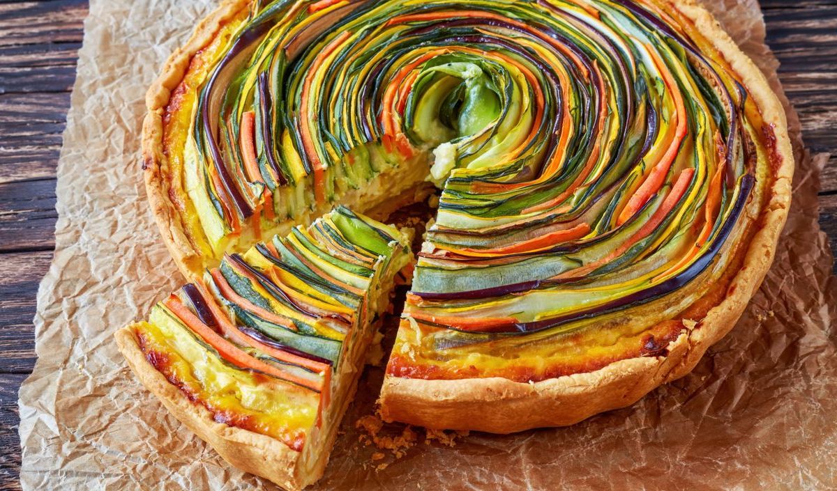 Bunte Spiral-Quiche mit verschiedenem Gemüse auf Backpapier.