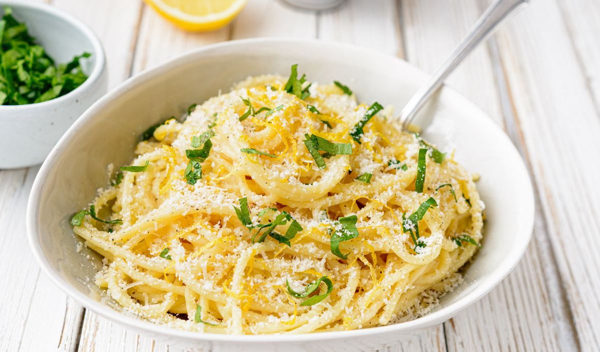 Weißer Teller mit Spaghetti, Zitronenabrieb und Parmesan.