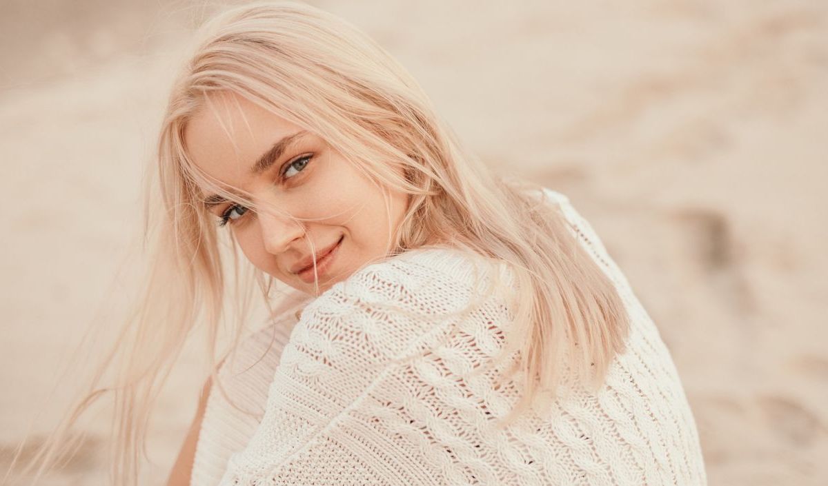 Frau mit blonden Haaren sitzt am Strand und schaut in die Kamera.