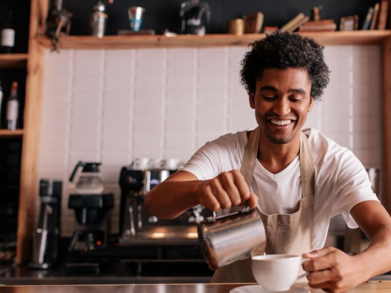 Barista bereitet lächelnd einen Cappuccino vor