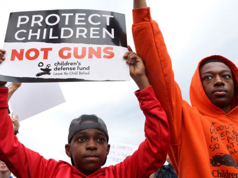 Ein kleiner Junge hält ein Protest-Schild hoch mit der Aufschrift "Schützt Kinder, nicht Waffen". 