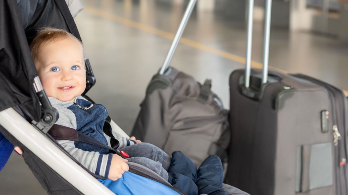 Kleines Baby sitzt im Kinderwagen, neben ihm stehen zwei Koffer.