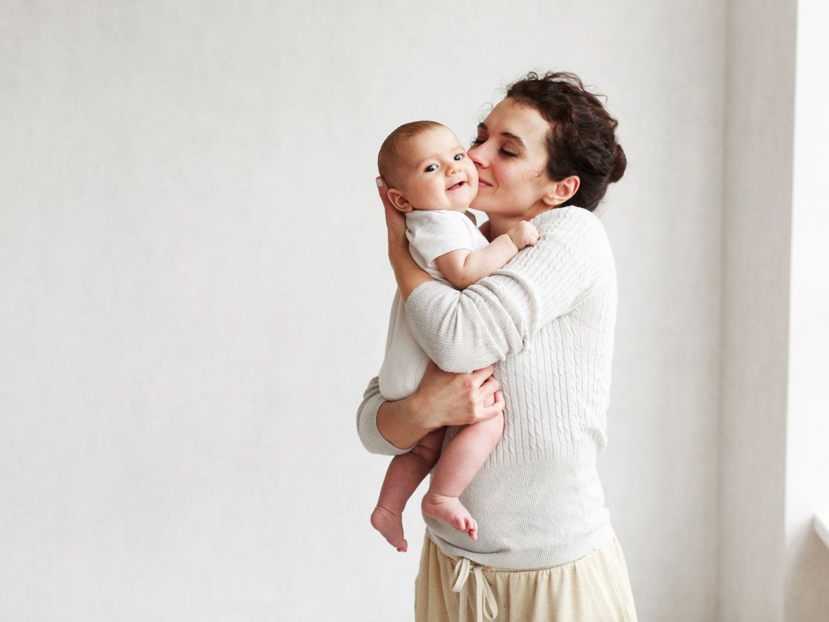 Frau hält Baby auf dem Arm und küsst es.