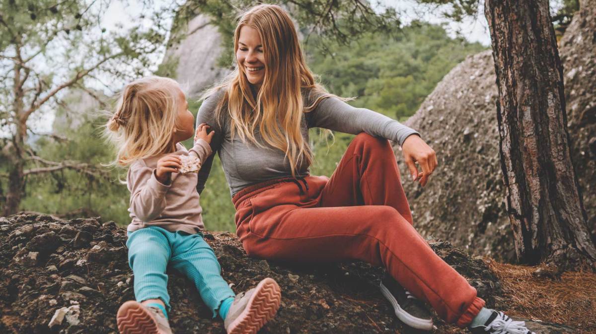 Mutter und Tochter sitzen in lockerer Freizeitmode in einem Wald und machen Pause.