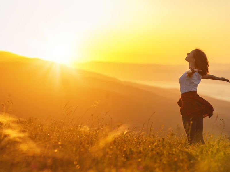 Frau mit ausgebreiteten Armen im Sonnenuntergang 