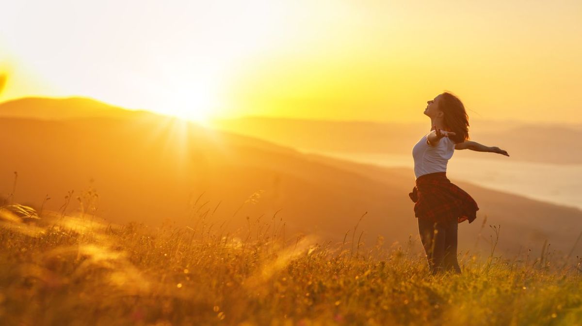 Frau mit ausgebreiteten Armen im Sonnenuntergang 