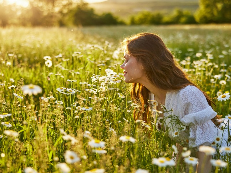 Frau auf Wiese, die an Blumen riecht