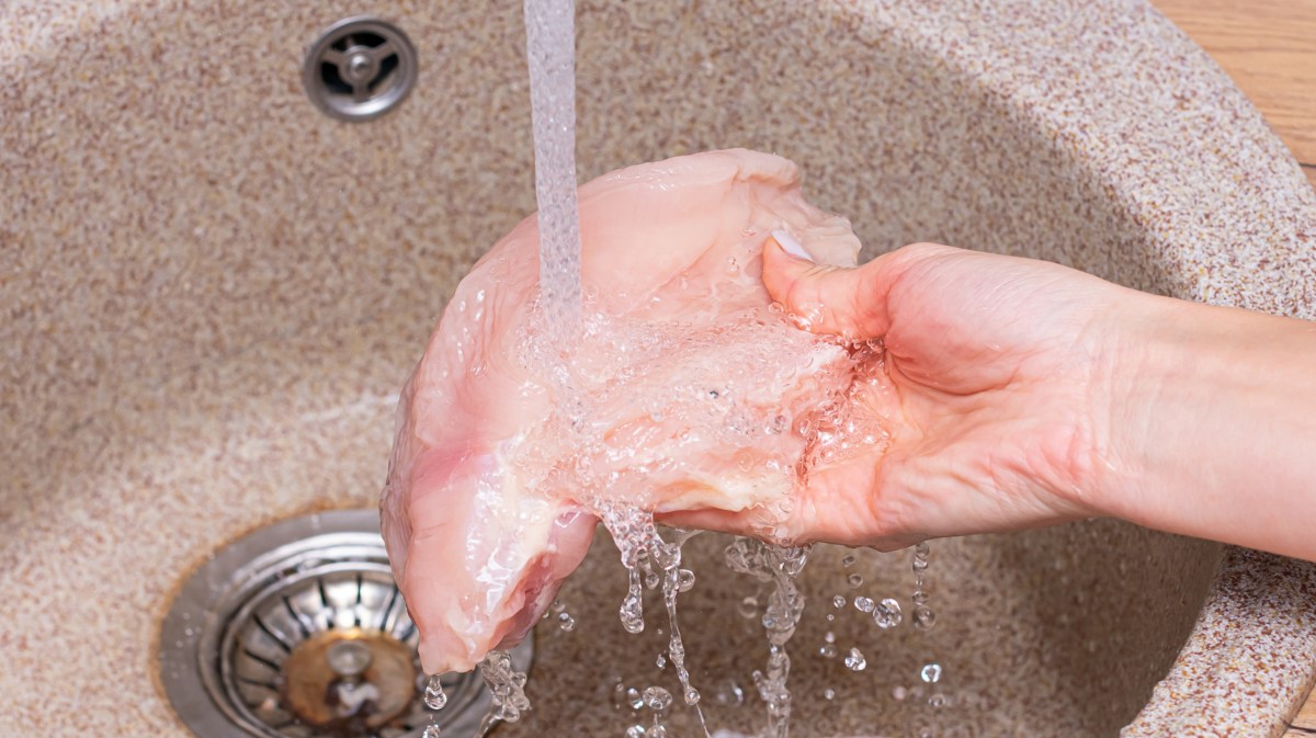 Person spült Hühnerbrust unter dem Wasserhahn ab.