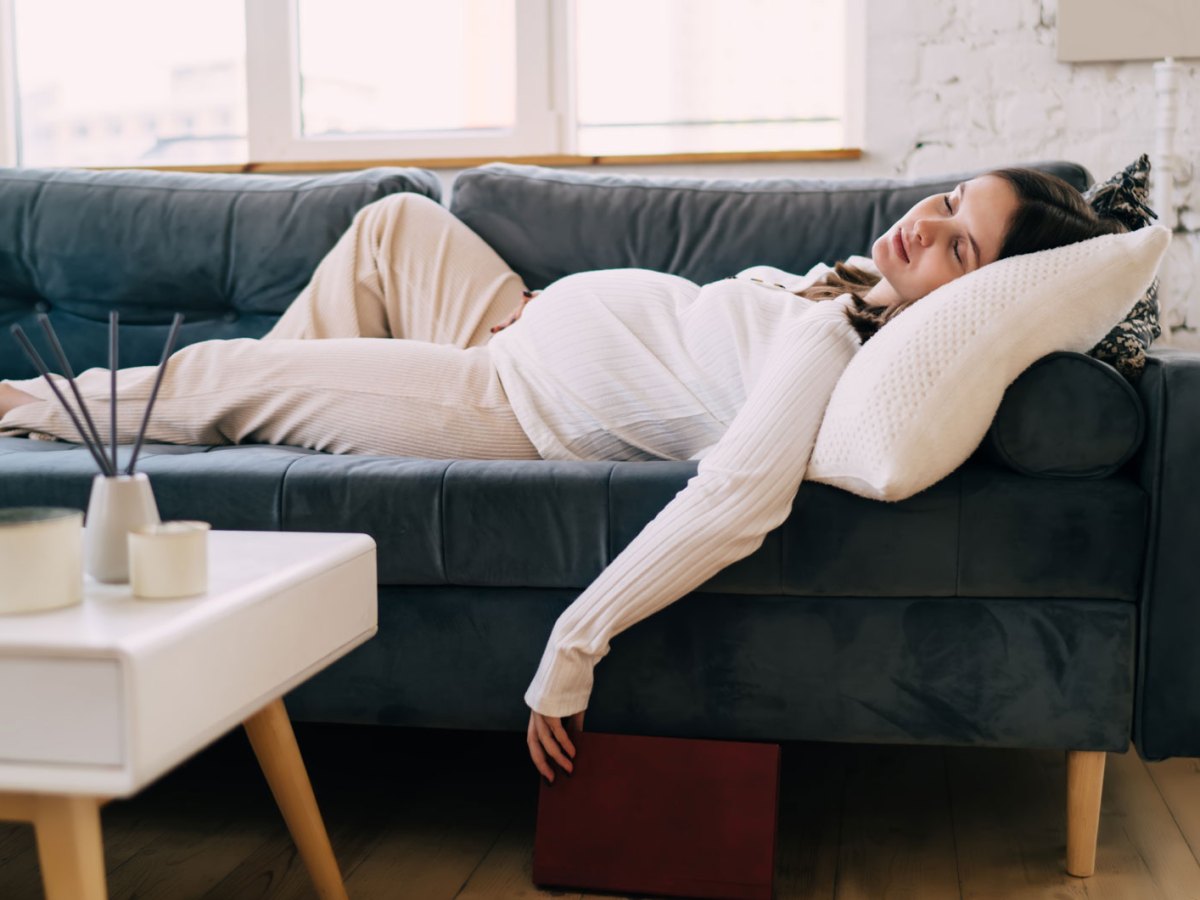 Schwangere Frau liegt sehr erschöpft auf dem Sofa und schläft.