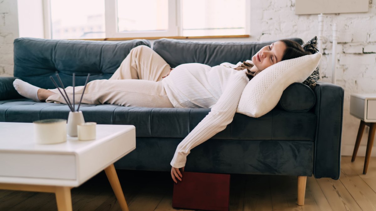 Schwangere Frau liegt sehr erschöpft auf dem Sofa und schläft.