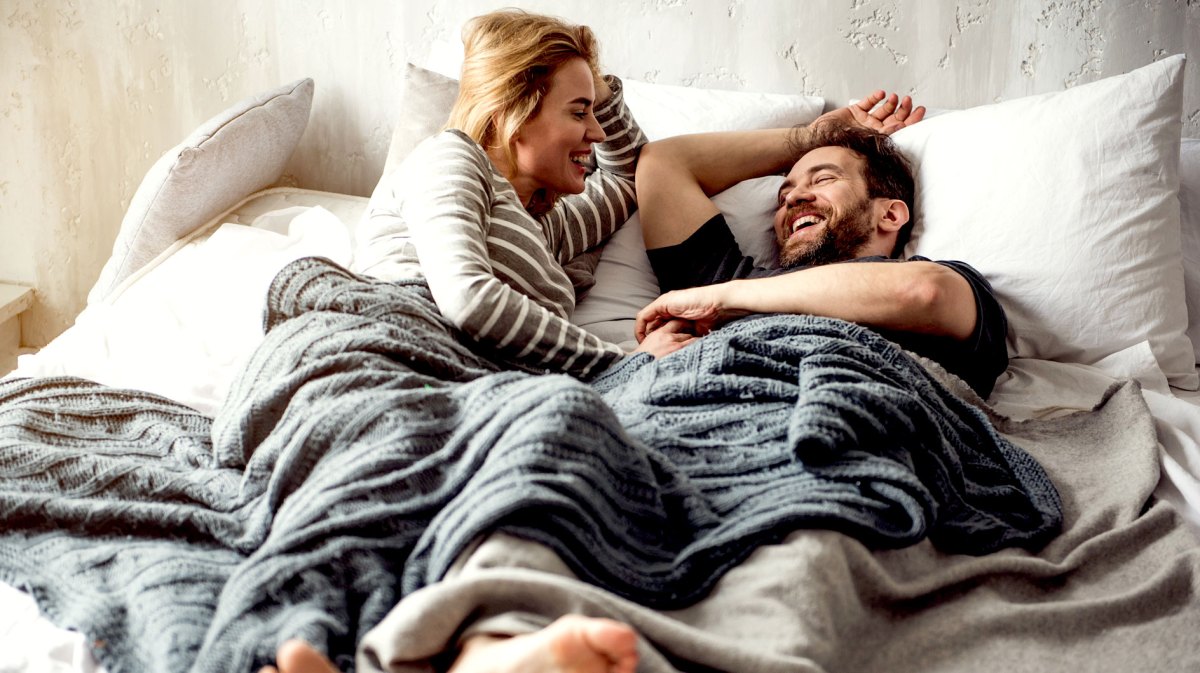 Mann und Frau liegen entspannt und lachend im Bett nebeneinander und unterhalten sich.