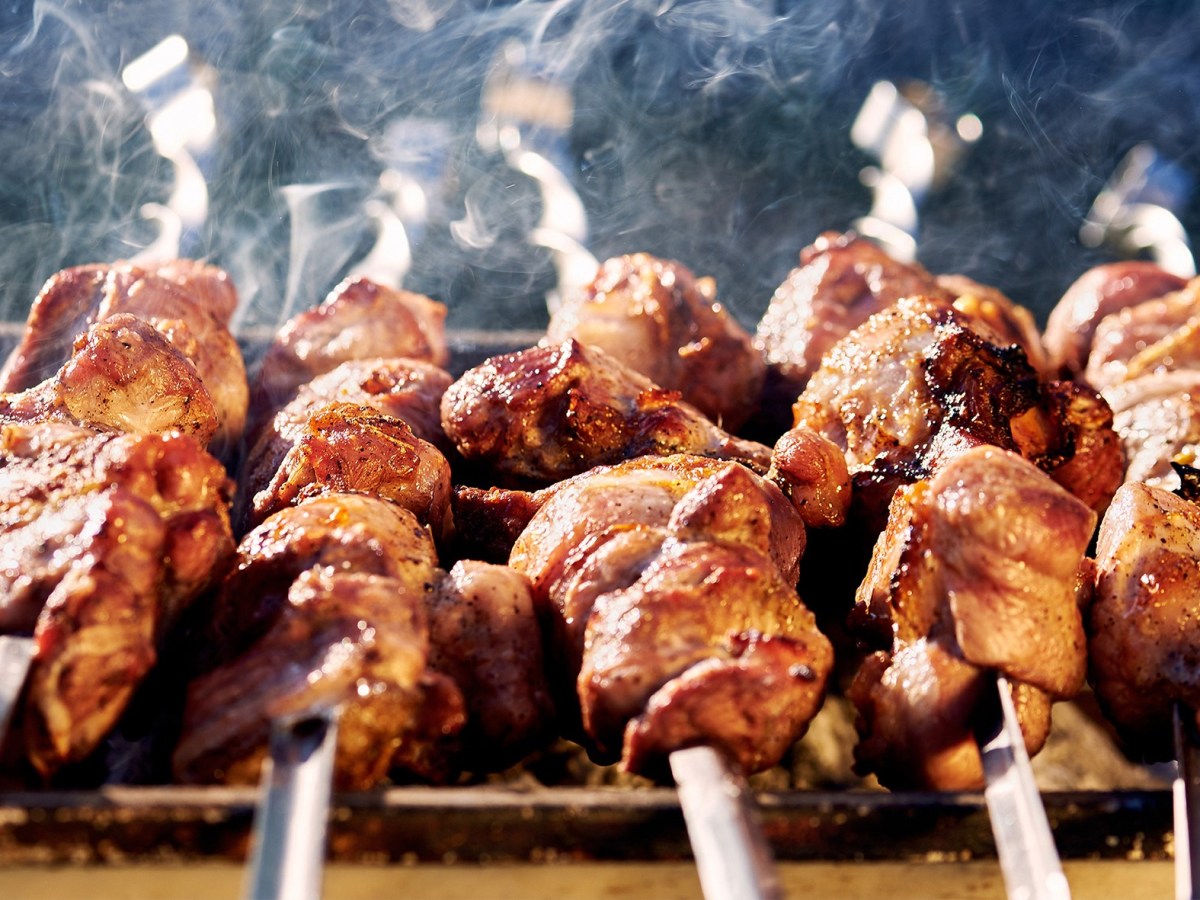 Original Schaschlikspieße vom Grill auf Grillplatte vor dunklem Hintergrund mit Rauschschwaden. Frontalansicht.