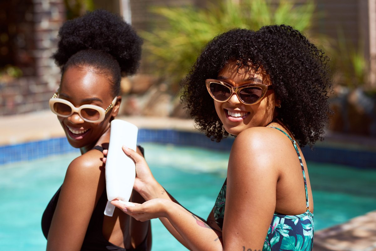 Zwei Frauen, die sich am Pool mit Sonnencreme eincremen