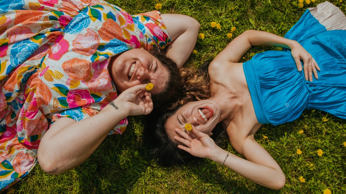 Frau und Mann auf einer Wiese, die lachen und nach oben in die Kamera schauen.