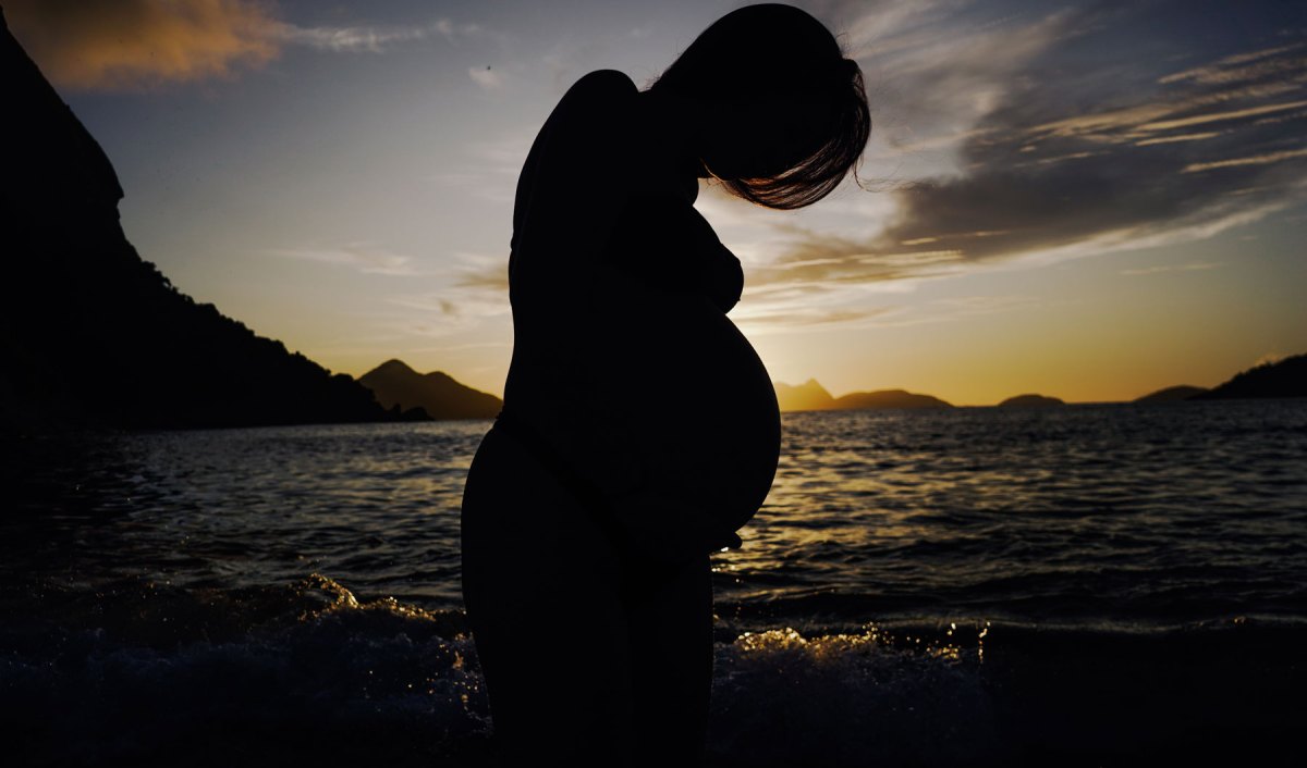 schwangere Frau vor einem Sonnenuntergang über dem Meer