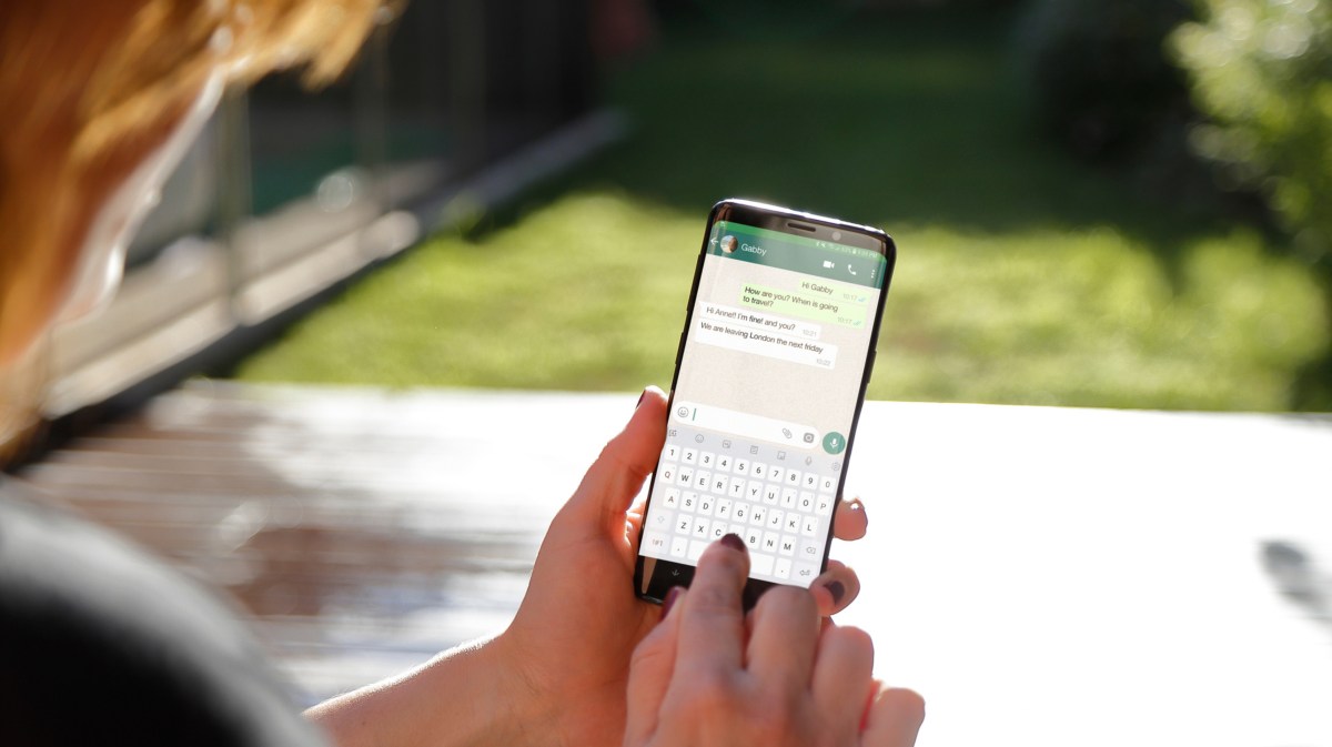 Frau draußen im Garten am Handy, die WhatsApp Chat schreibt