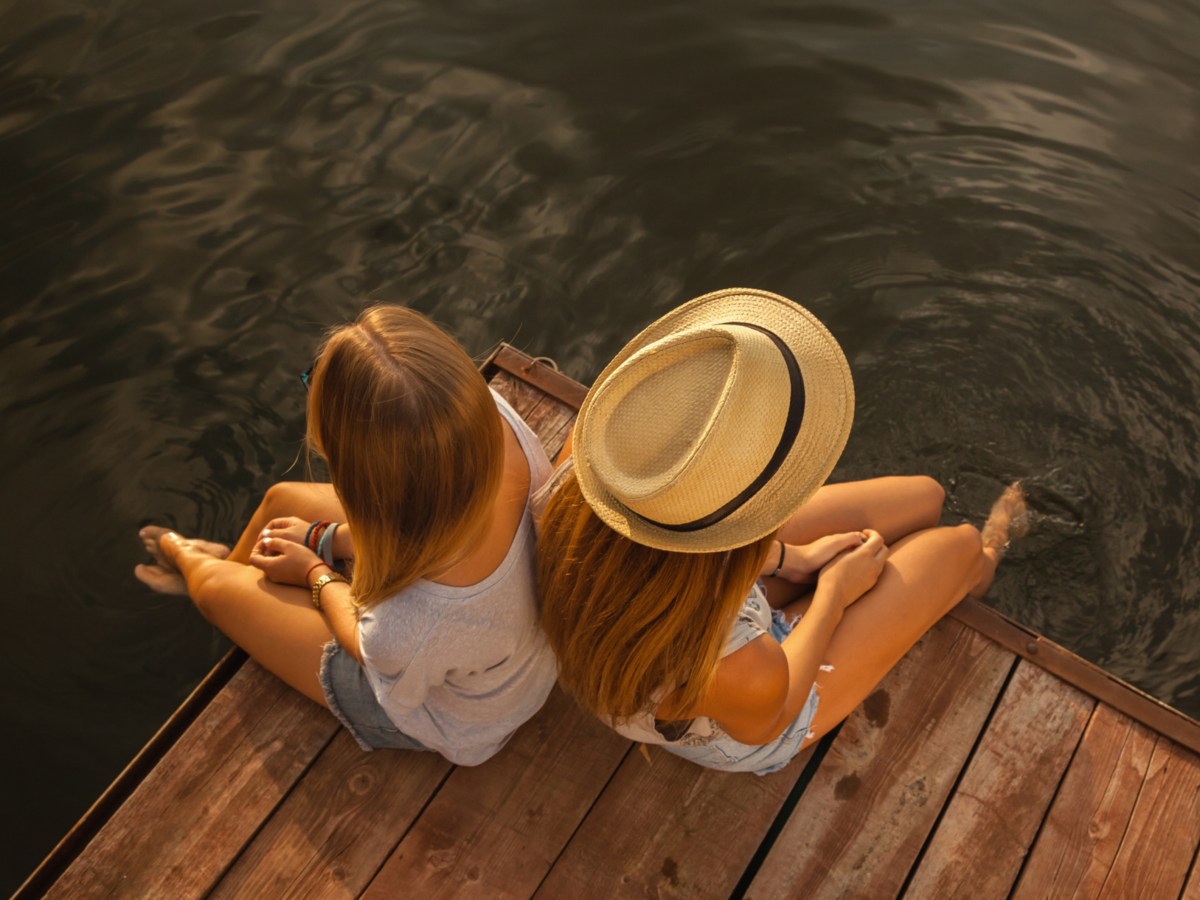 Zwei Frauen am Ufer auf Steg, die in die entgegengesetzte Richtung schauen und sitzen