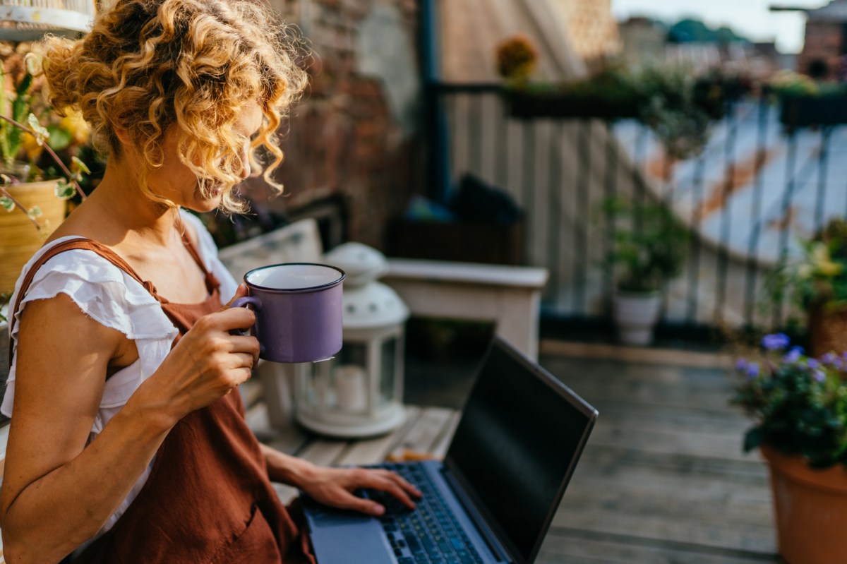 Frau sitzt mit einem Laptop auf dem Balkon und macht Home Office im Freien