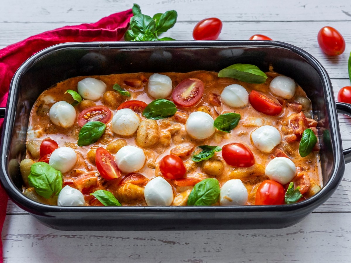 Ofen Gnocchi mit Tomate und Mozzarella in schwarzer Auflaufform auf weißem Holz.