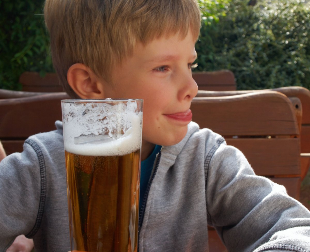 Etwa 10-jähriger Junge sitzt vor einem großen Glas Bier.