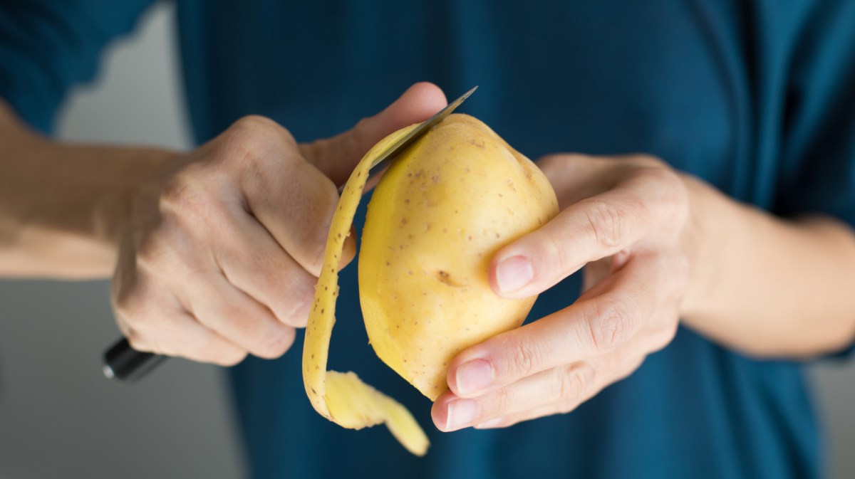 Person mit blauem Oberteil hält Kartoffel in den Händen und schält sie.