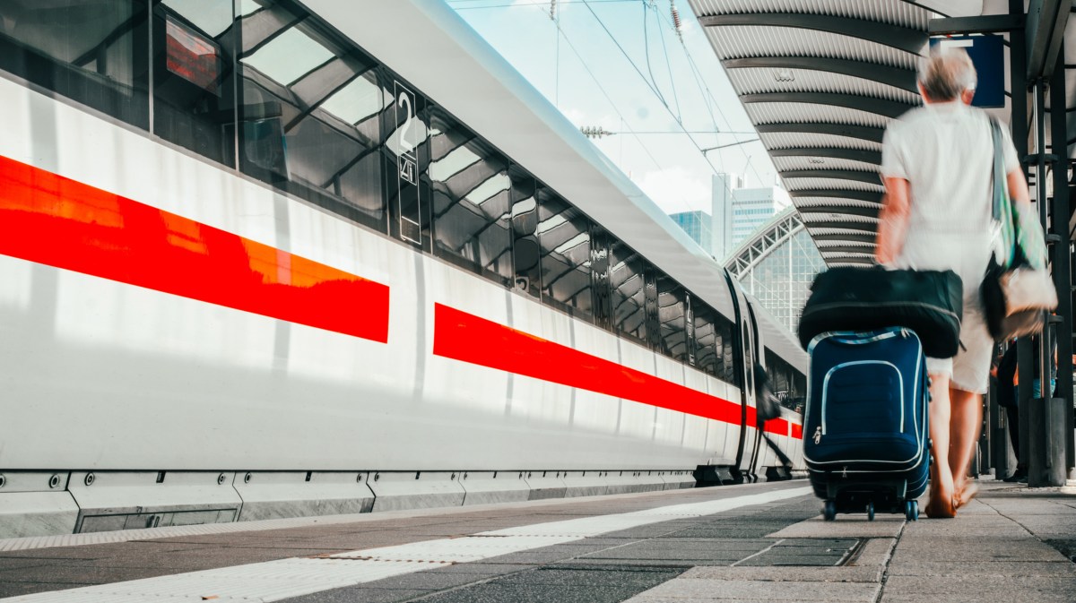 Zug der deutschen Bahn, der gerade einfährt, mit einem Mann am rechten Bildrand, der seinen Koffer hinter sich herzieht