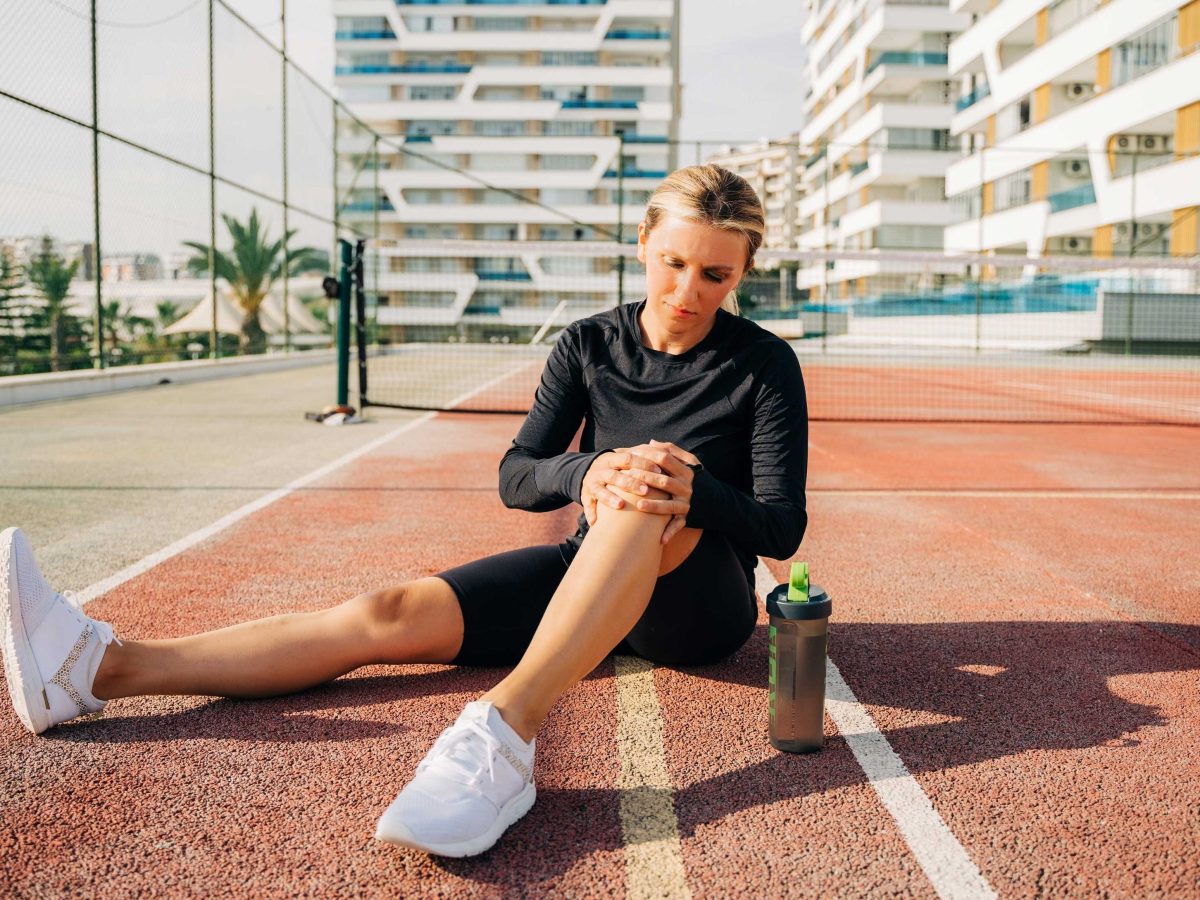 Athletische Frau hält sich das schmerzende Knie auf einem Tennisplatz