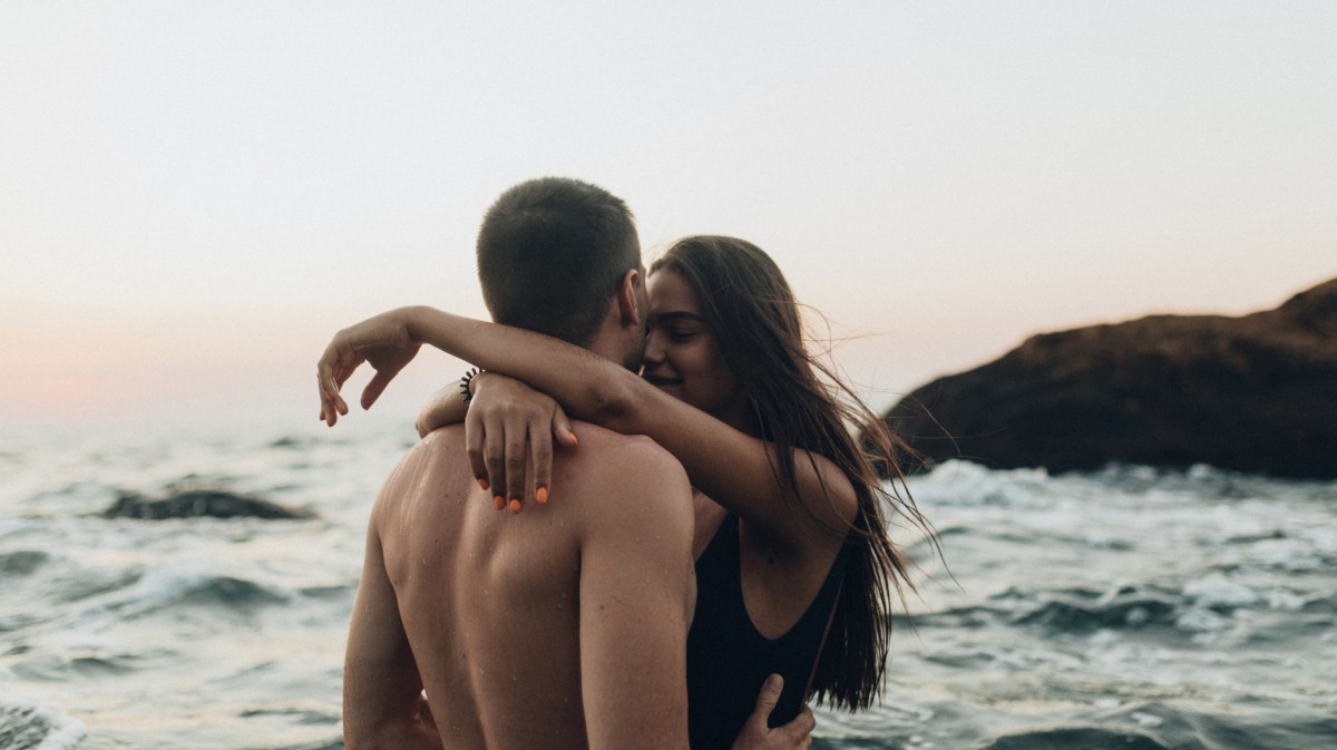 Pärchen am Strand, das sich umarmt, während im Hintergrund die Wellen zu sehen sind