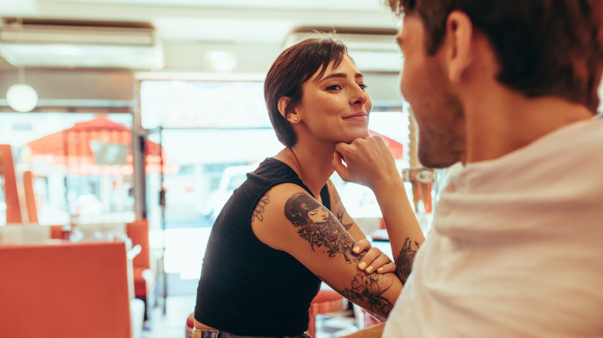 Frau mit Tattoos und kurzen Haaren in einem Waschsalon, die einen Mann gegenüber anlächelt und flirtet