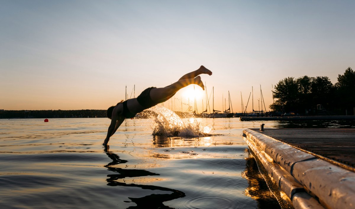 Eine Frau macht bei Sonnenuntergang einen Kopfsprung in einen See.