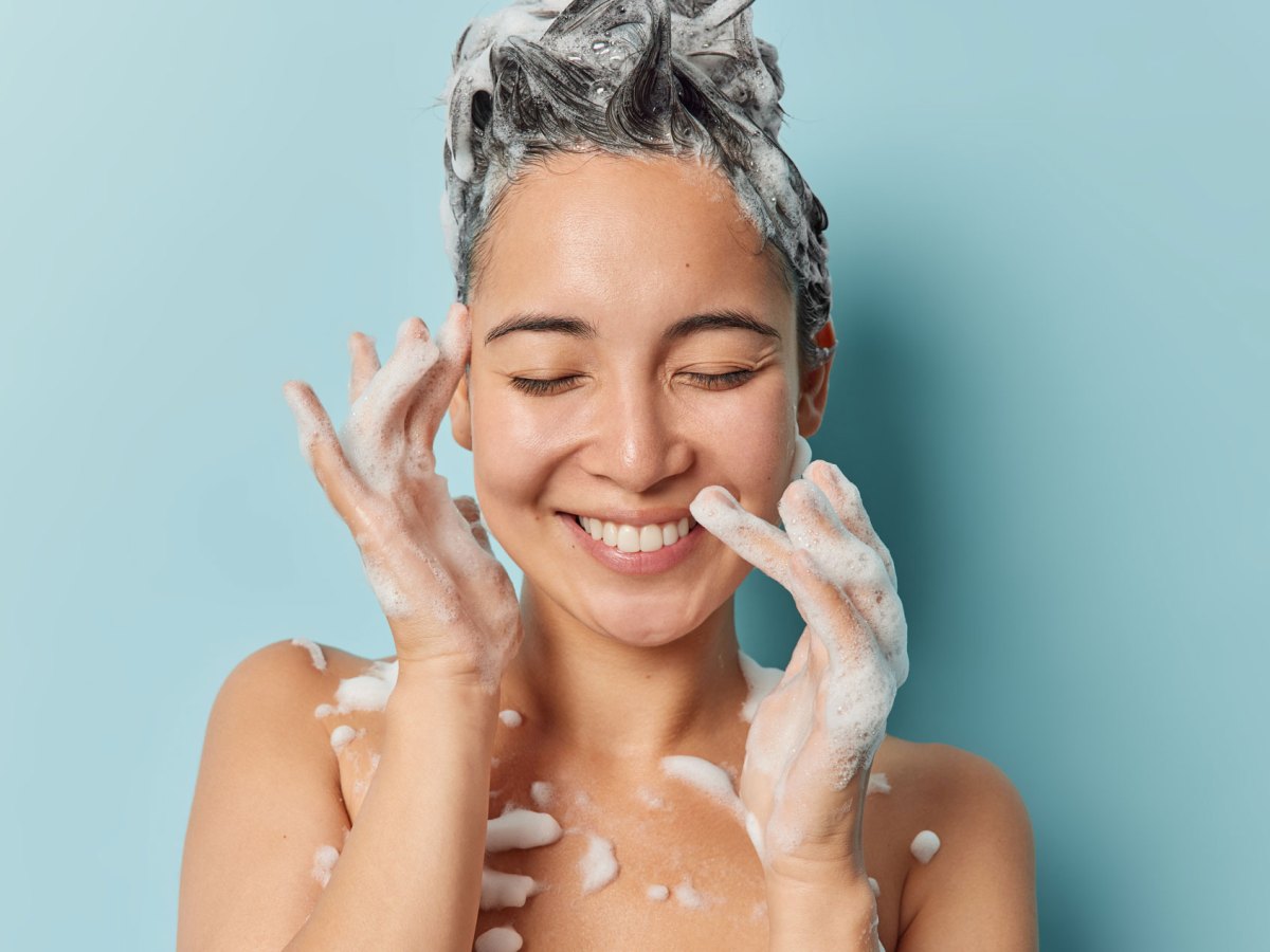 Junge Frau mit eingeschäumten Haaren unter der Dusche.