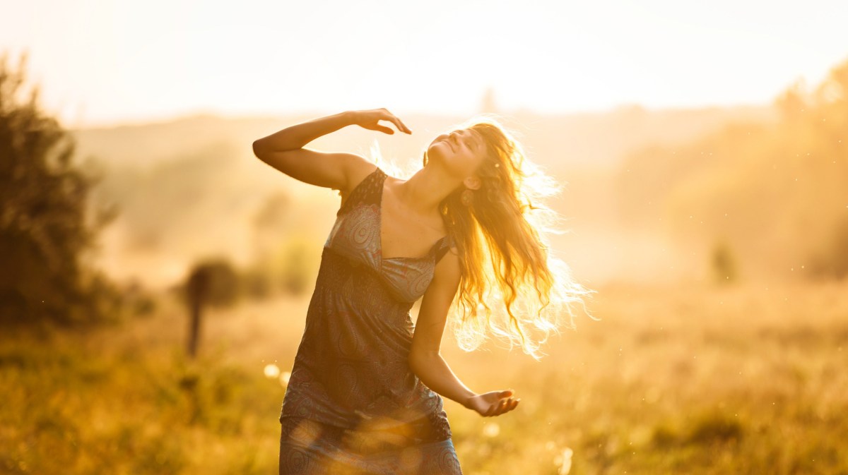 Frau tanzt in einem Feld bei untergehender Sonne.