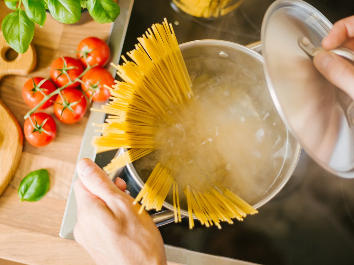 Person kocht Spagetti und öffnet den Topfdeckel. Es tritt Dampf aus.