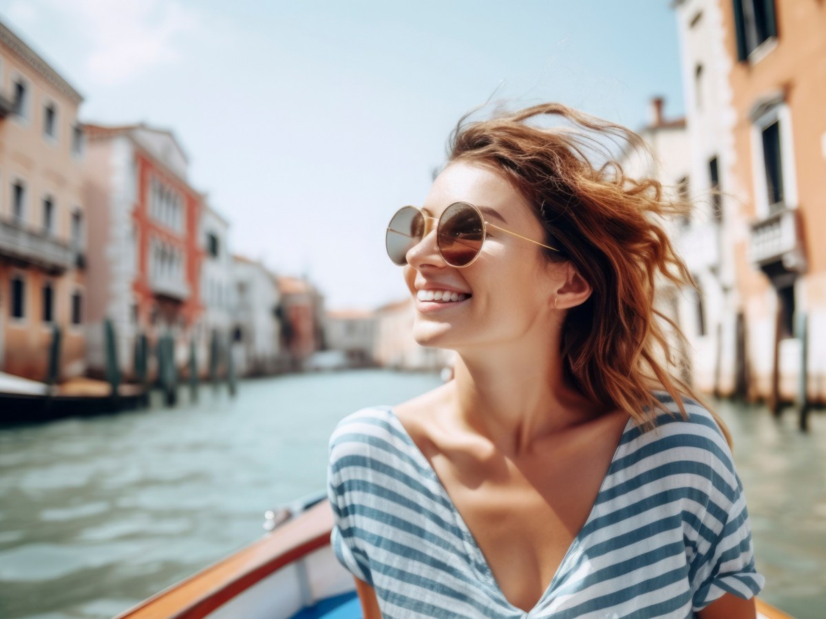 Frau mit Sonnenbrille und einem Streifen-Oberteil sitzt in einer Gracht in Venedig.