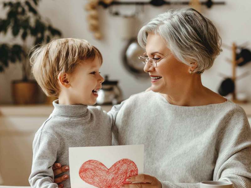 Oma und ihr Enkel. Die Oma hält ein selbst gemaltes rotes Herz in der Hand.