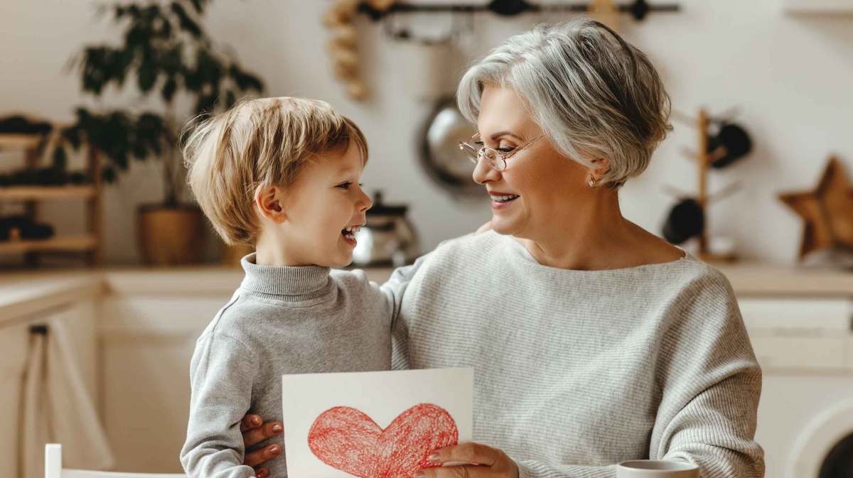 Oma und ihr Enkel. Die Oma hält ein selbst gemaltes rotes Herz in der Hand.