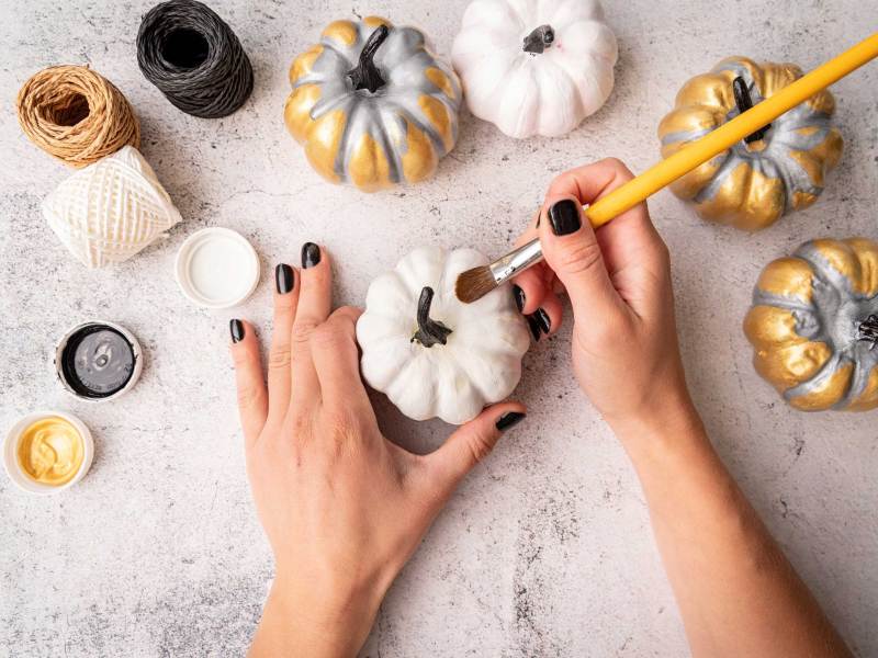 Weibliche Hände mit schwarzen Nägeln malen Kürbisse für Halloween