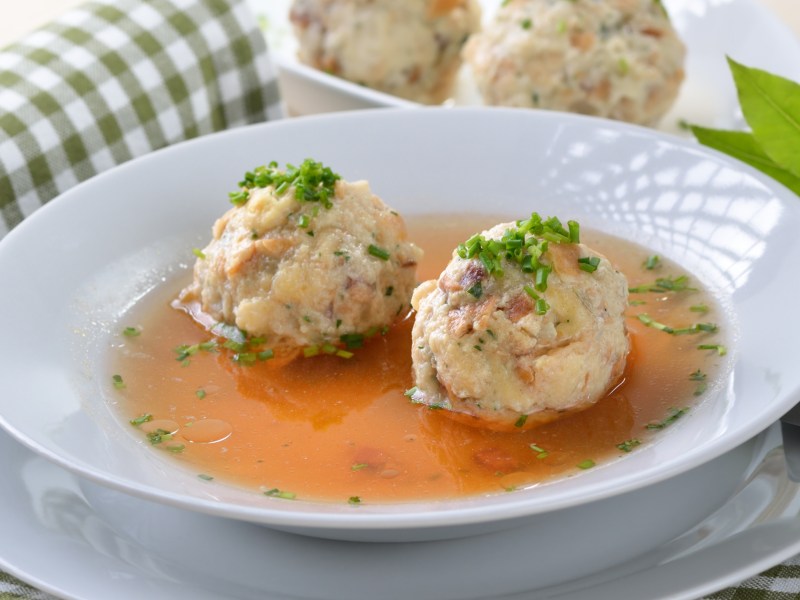 Tiroler Speckknödelsuppe in weißem Suppenteller.