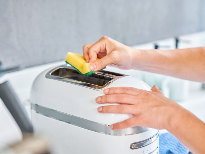 Hände, die Toaster reinigen