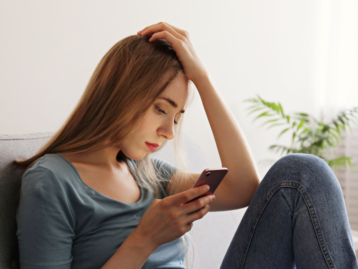 Frau mit Handy auf der Couch, die gelangweilt schaut