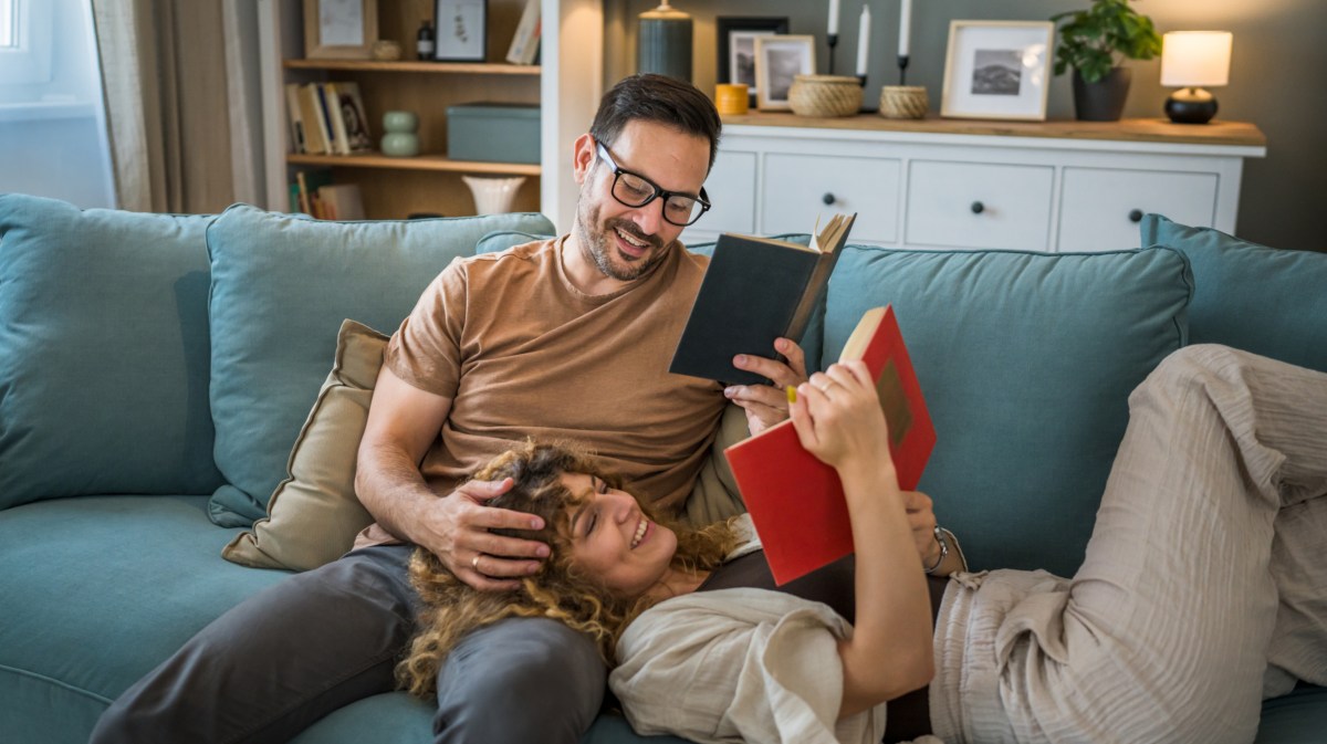 Paar, das mit Büchern auf der Couch liegt, während der Mann sitzt und die Frau auf seinem Schoß liegt