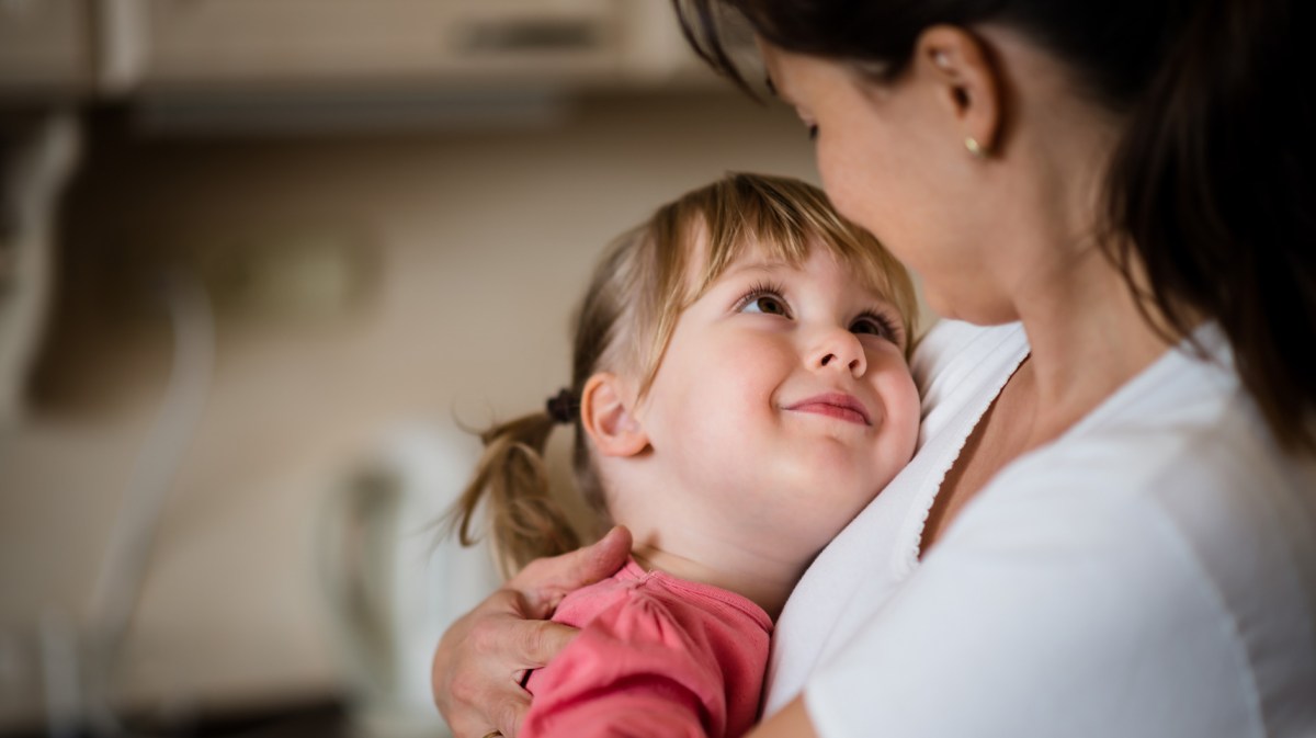 Tochter, ca. 5 Jahre alt, liegt in den Armen ihrer Mama und schaut sie ganz verliebt und glücklich an.