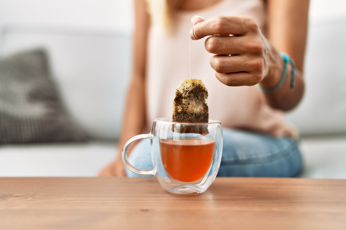 Eine Frau zieht einen Teebeutel aus einer Teetasse.