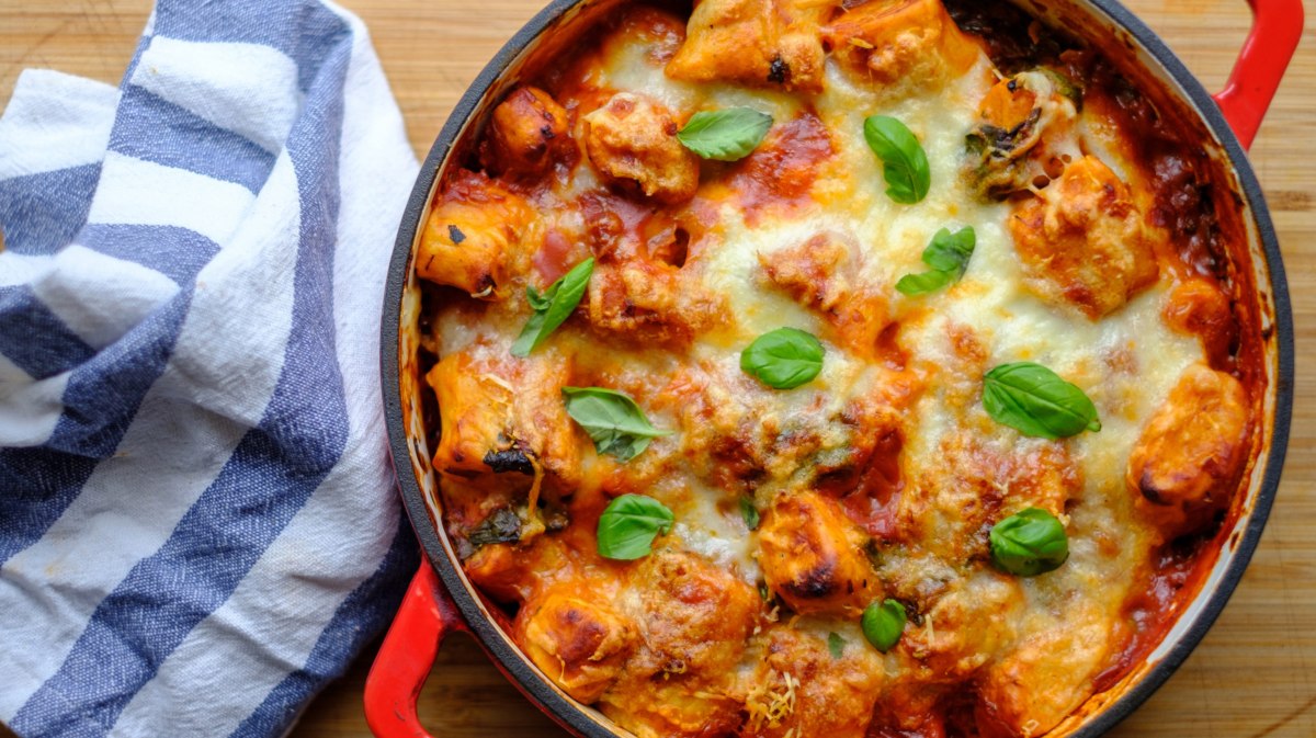 Auflauf mit Gnocchi, Tomatensoße und Käse in rotem feuerfesten Topf.