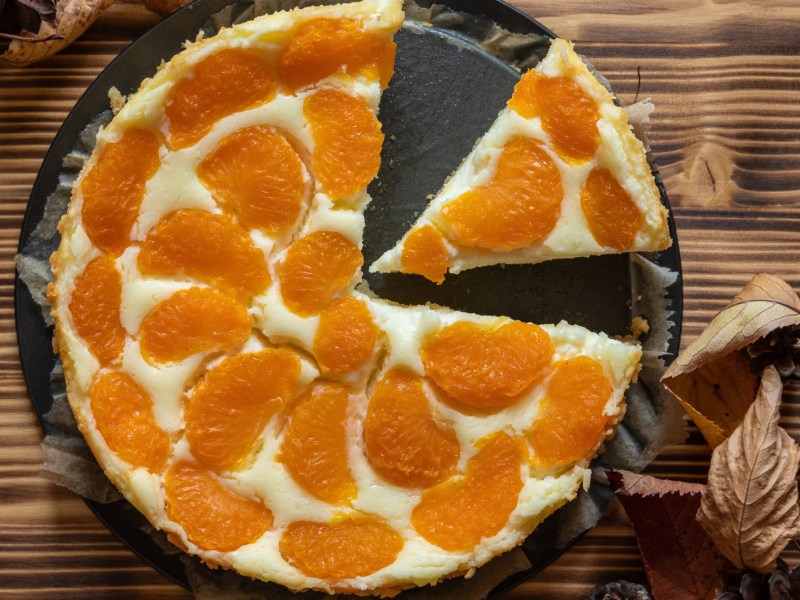 Schmandkuchen mit Mandarinen in einer Springform auf einem Holztisch.