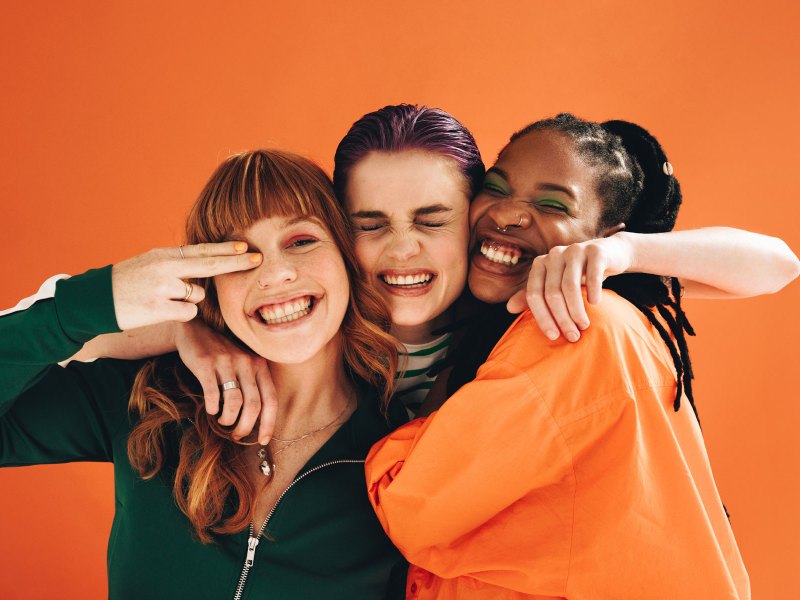 Drei Frauen umarmen sich vor einer orangefarbenen Wand