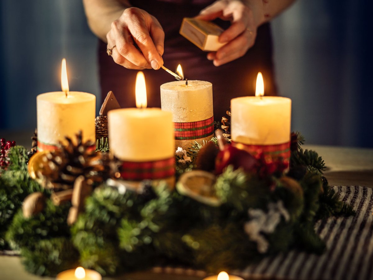 Eine Frau zündet die vierte Kerze eines Adventskalenders an.