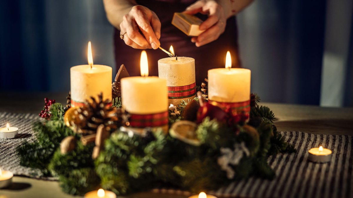 Eine Frau zündet die vierte Kerze eines Adventskalenders an.